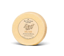 Load image into Gallery viewer, A round, pale yellow soap bar standing upright on its side, featuring a circular beige label with the brand name 'Bee Vee Clean by BVTalks' and the scent 'HUSH'.