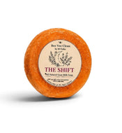 An orange-brown circular soap bar with a cream-colored paper label reading 'The Shift' by Bee Vee Clean, photographed on a white background with a soft shadow.